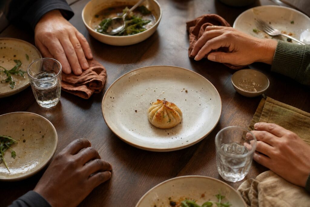 Four diners pause around a shared plate holding one final golden dumpling.