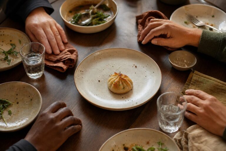 Four diners pause around a shared plate holding one final golden dumpling.